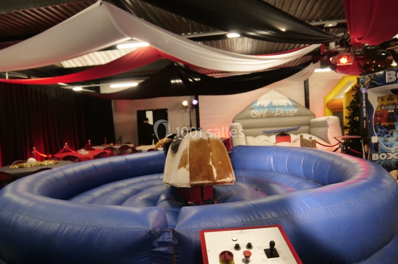 Taureau mécanique au centre d'une structure gonflable bleue, installé dans une salle décorée de tentures rouges et blanches.