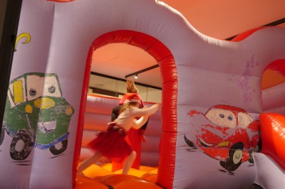 Des enfants colorient des dessins autour d'une table ronde, entourés d'adultes dans un espace intérieur animé.