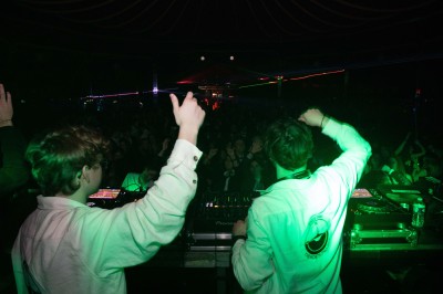 Des enfants colorient des dessins autour d'une table ronde, entourés d'adultes dans un espace intérieur animé.