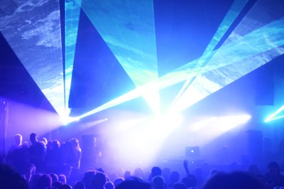 Des enfants colorient des dessins autour d'une table ronde, entourés d'adultes dans un espace intérieur animé.