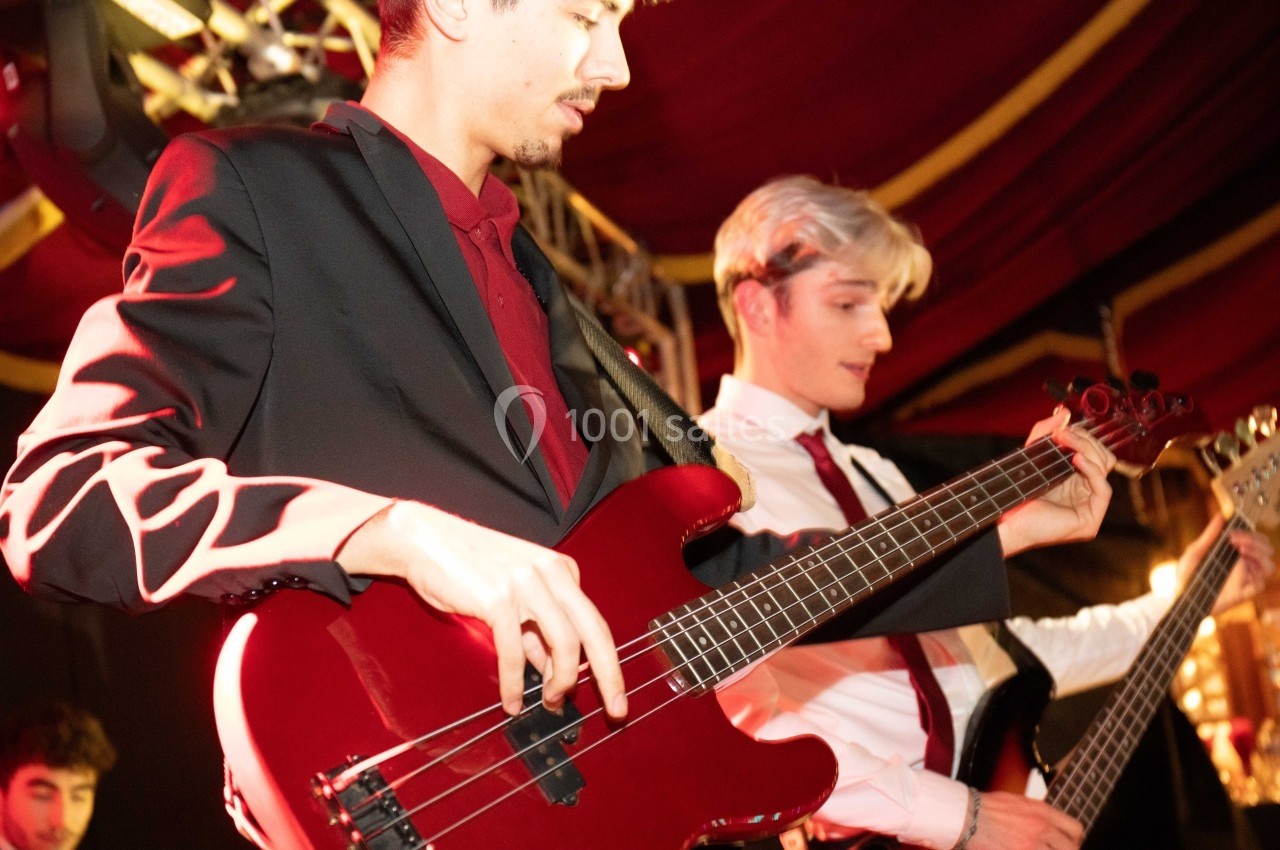 Deux musiciens jouent de la guitare basse sur une scène éclairée, dans une ambiance de concert.