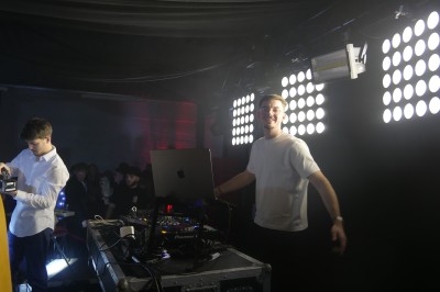 Des enfants colorient des dessins autour d'une table ronde, entourés d'adultes dans un espace intérieur animé.