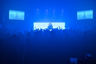 Des enfants colorient des dessins autour d'une table ronde, entourés d'adultes dans un espace intérieur animé.