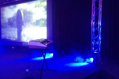 Des enfants colorient des dessins autour d'une table ronde, entourés d'adultes dans un espace intérieur animé.