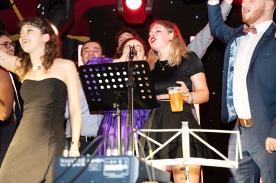 Des enfants colorient des dessins autour d'une table ronde, entourés d'adultes dans un espace intérieur animé.