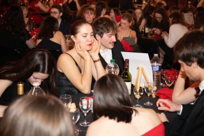 Des enfants colorient des dessins autour d'une table ronde, entourés d'adultes dans un espace intérieur animé.