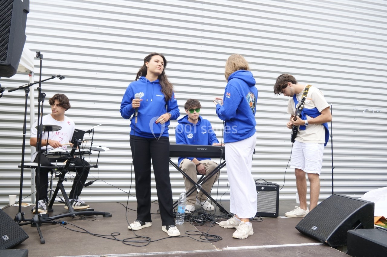 Un groupe de jeunes musiciens joue sur une petite scène extérieure devant un mur métallique.