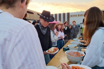 Des enfants colorient des dessins autour d'une table ronde, entourés d'adultes dans un espace intérieur animé.