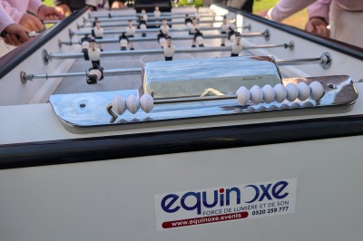 Des enfants colorient des dessins autour d'une table ronde, entourés d'adultes dans un espace intérieur animé.