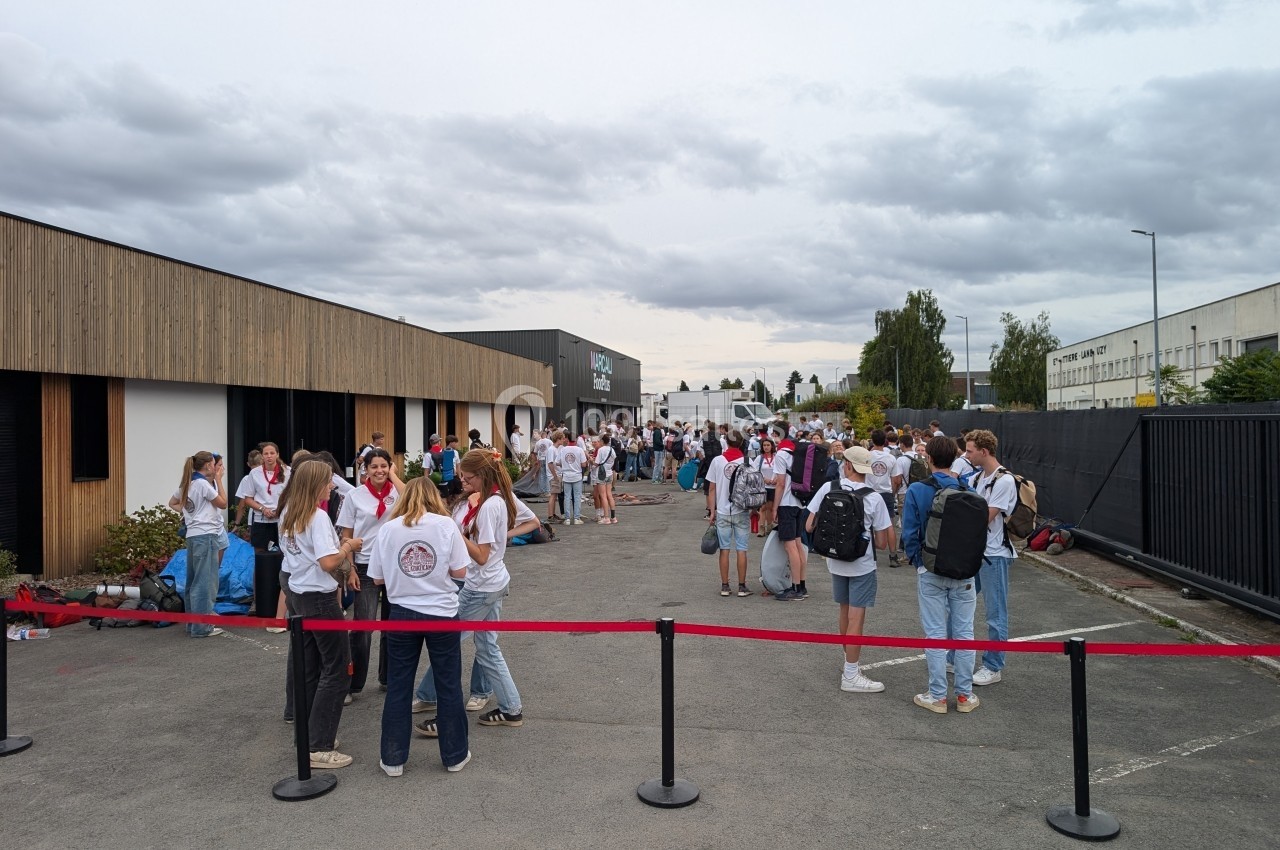 Des personnes rassemblées à l'extérieur d'un bâtiment moderne, discutant par petits groupes sous un ciel nuageux.