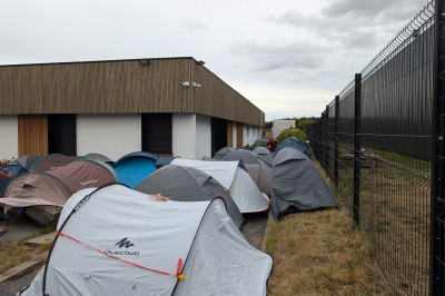 Des enfants colorient des dessins autour d'une table ronde, entourés d'adultes dans un espace intérieur animé.