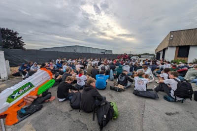 Des enfants colorient des dessins autour d'une table ronde, entourés d'adultes dans un espace intérieur animé.