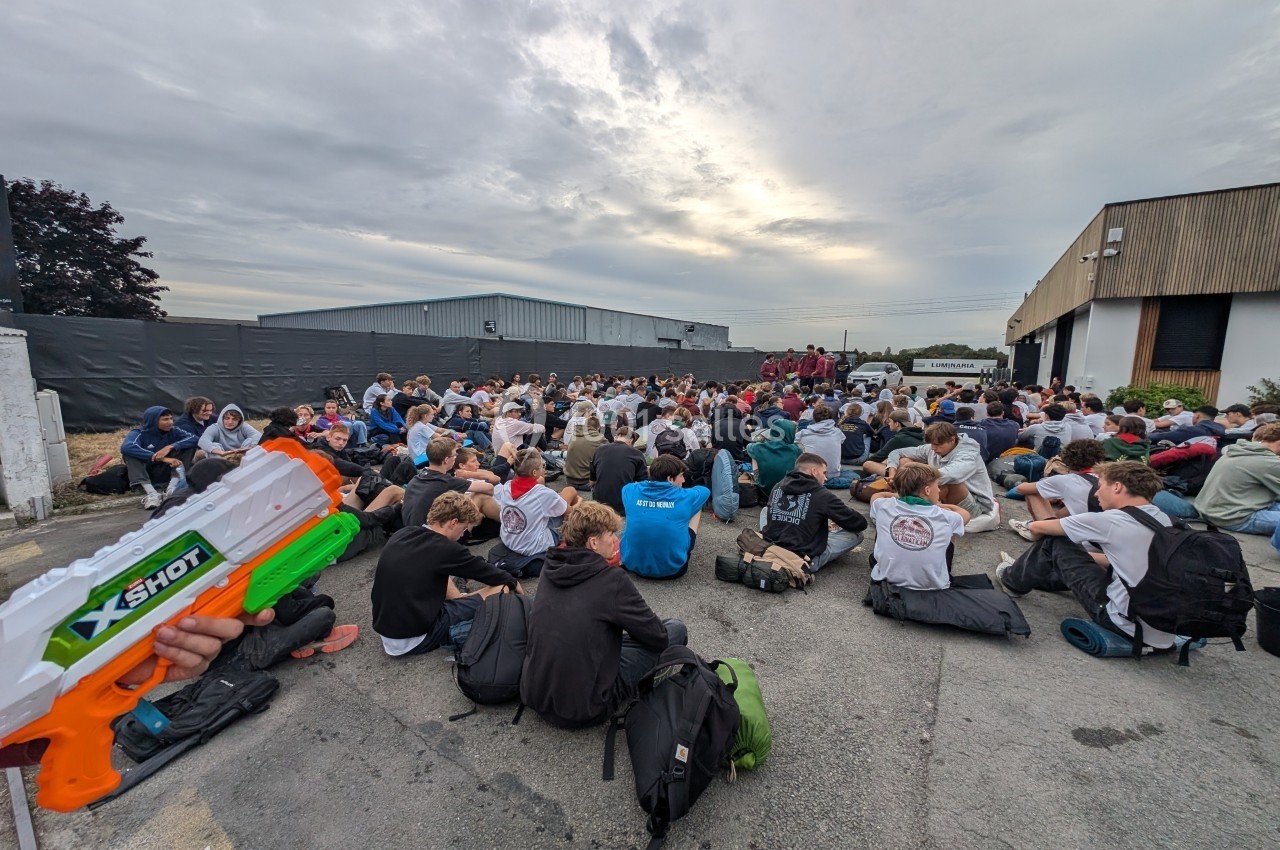 Un groupe de personnes assises à l'extérieur sur un sol en béton, avec un pistolet à eau visible au premier plan.