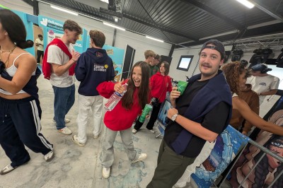 Des enfants colorient des dessins autour d'une table ronde, entourés d'adultes dans un espace intérieur animé.