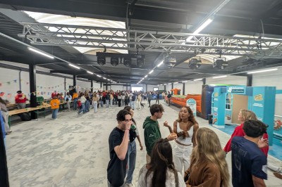 Des enfants colorient des dessins autour d'une table ronde, entourés d'adultes dans un espace intérieur animé.