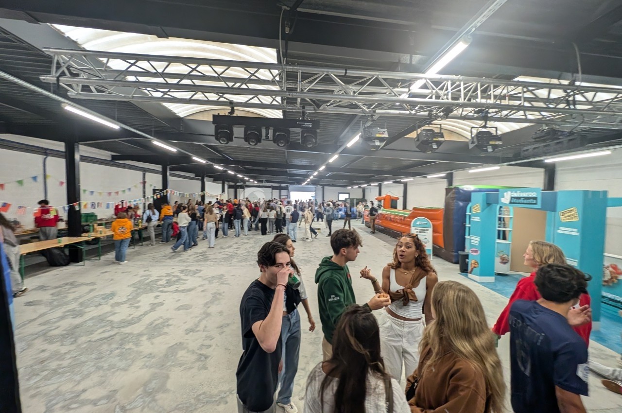 Des personnes discutent et se déplacent dans un grand espace intérieur éclairé, aménagé avec des stands et des décorations.