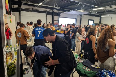 Des enfants colorient des dessins autour d'une table ronde, entourés d'adultes dans un espace intérieur animé.