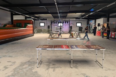 Des enfants colorient des dessins autour d'une table ronde, entourés d'adultes dans un espace intérieur animé.