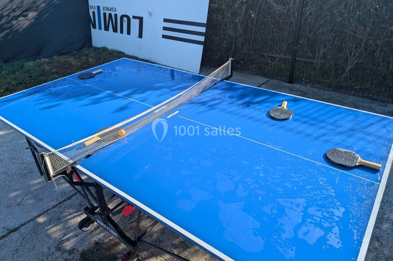 Table de ping-pong bleue en extérieur avec deux raquettes posées, surface mouillée par la rosée.