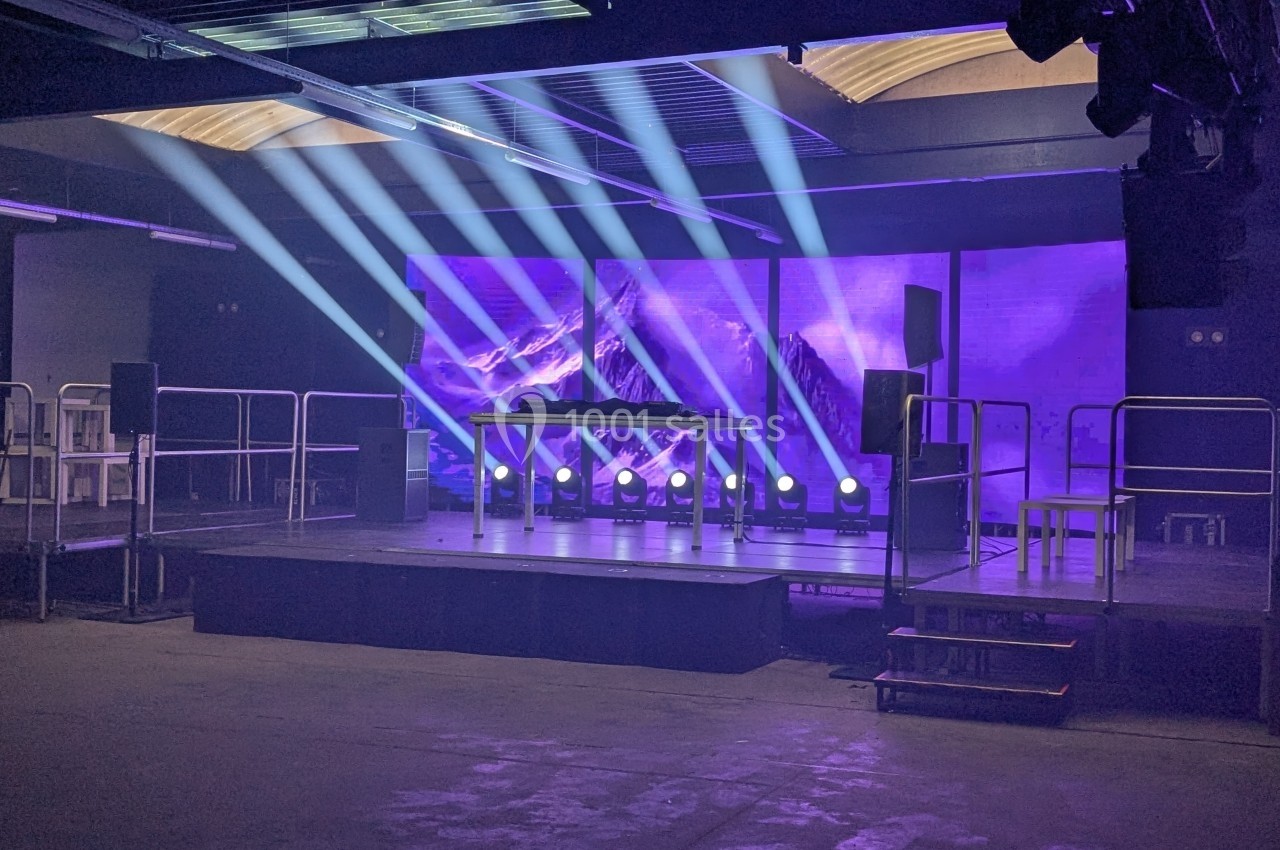 Scène vide avec éclairage violet et projecteurs, entourée de haut-parleurs et de plateformes métalliques.