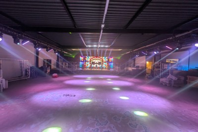 Des enfants colorient des dessins autour d'une table ronde, entourés d'adultes dans un espace intérieur animé.