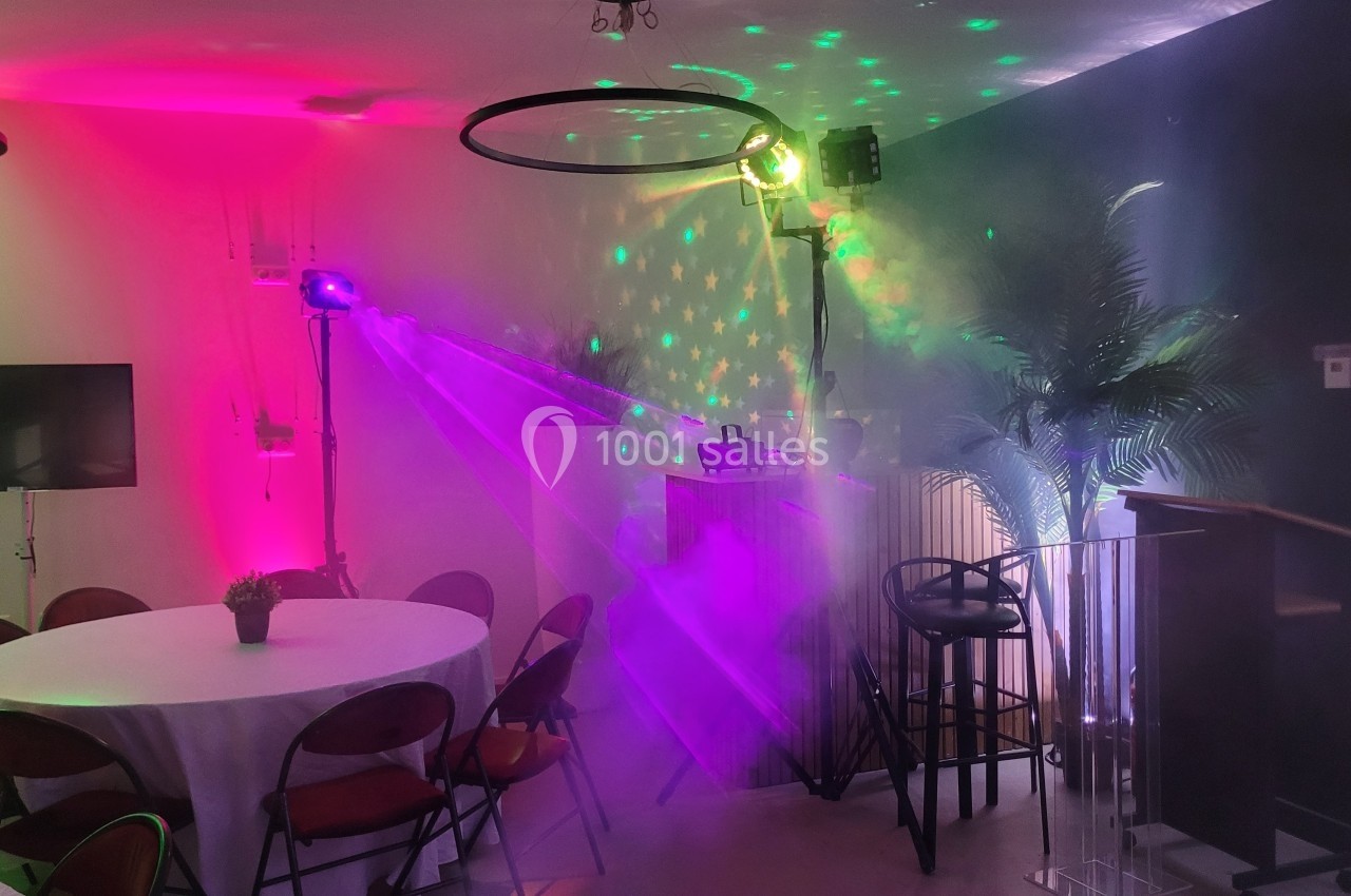 Salle décorée avec des lumières colorées, des tables rondes, des chaises pliantes et un effet de fumée.