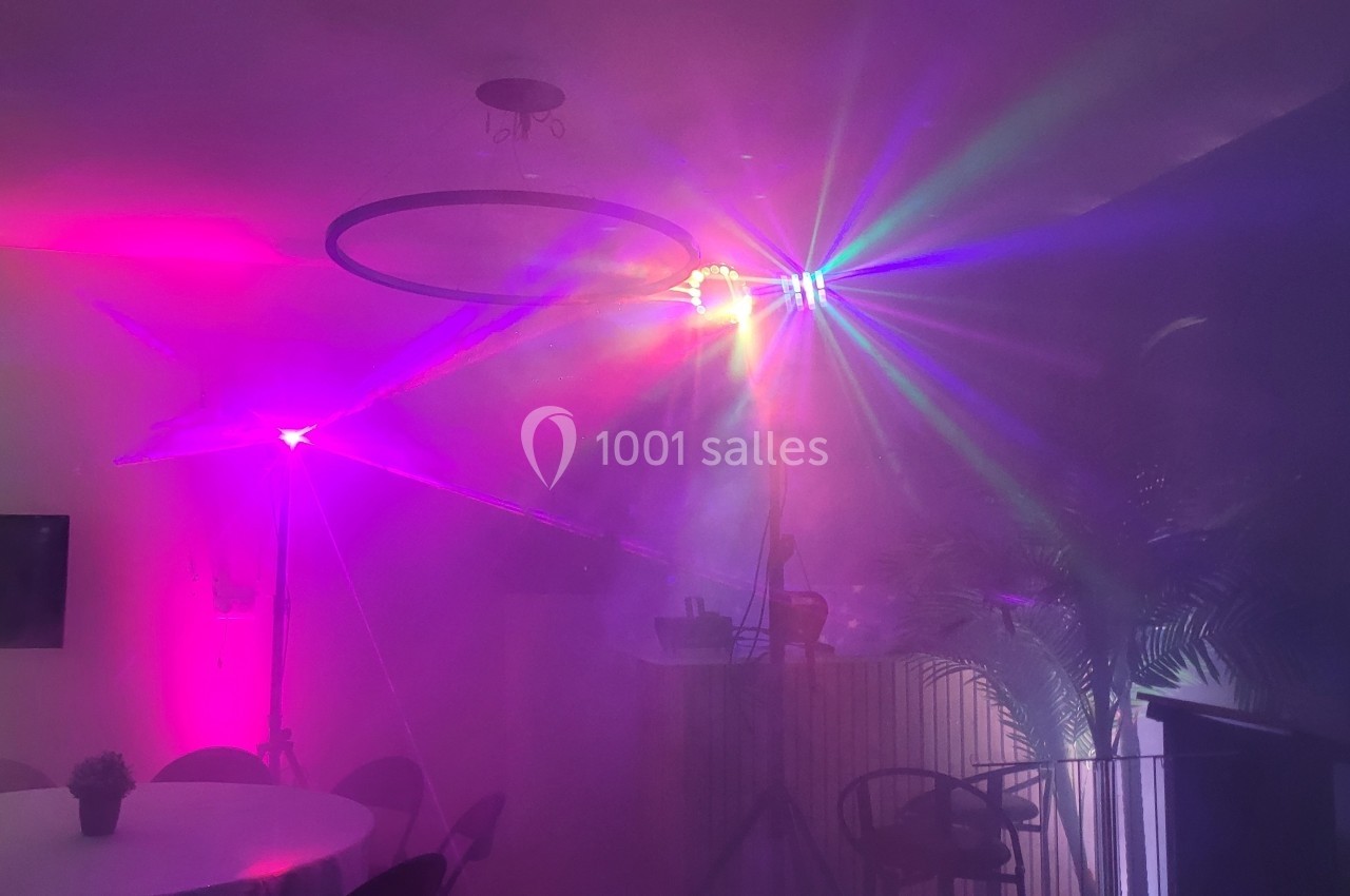 Effets lumineux colorés et fumée dans une pièce sombre avec des meubles et des plantes en arrière-plan.