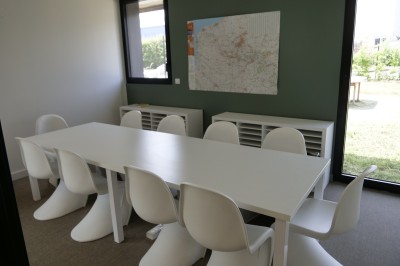 Des enfants colorient des dessins autour d'une table ronde, entourés d'adultes dans un espace intérieur animé.