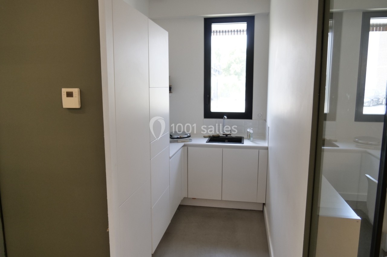 Cuisine moderne et étroite avec meubles blancs, évier sous une fenêtre et sol en béton gris.