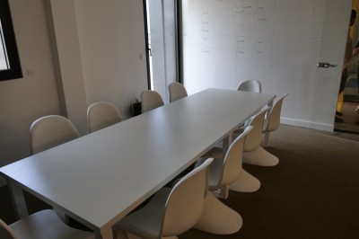 Des enfants colorient des dessins autour d'une table ronde, entourés d'adultes dans un espace intérieur animé.