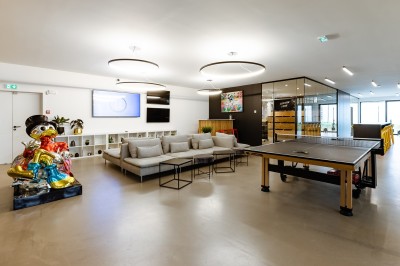 Des enfants colorient des dessins autour d'une table ronde, entourés d'adultes dans un espace intérieur animé.