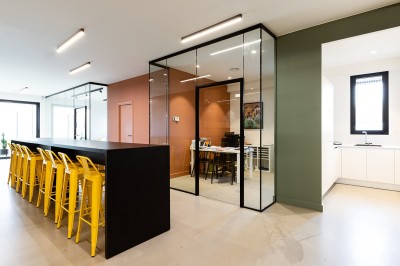 Des enfants colorient des dessins autour d'une table ronde, entourés d'adultes dans un espace intérieur animé.