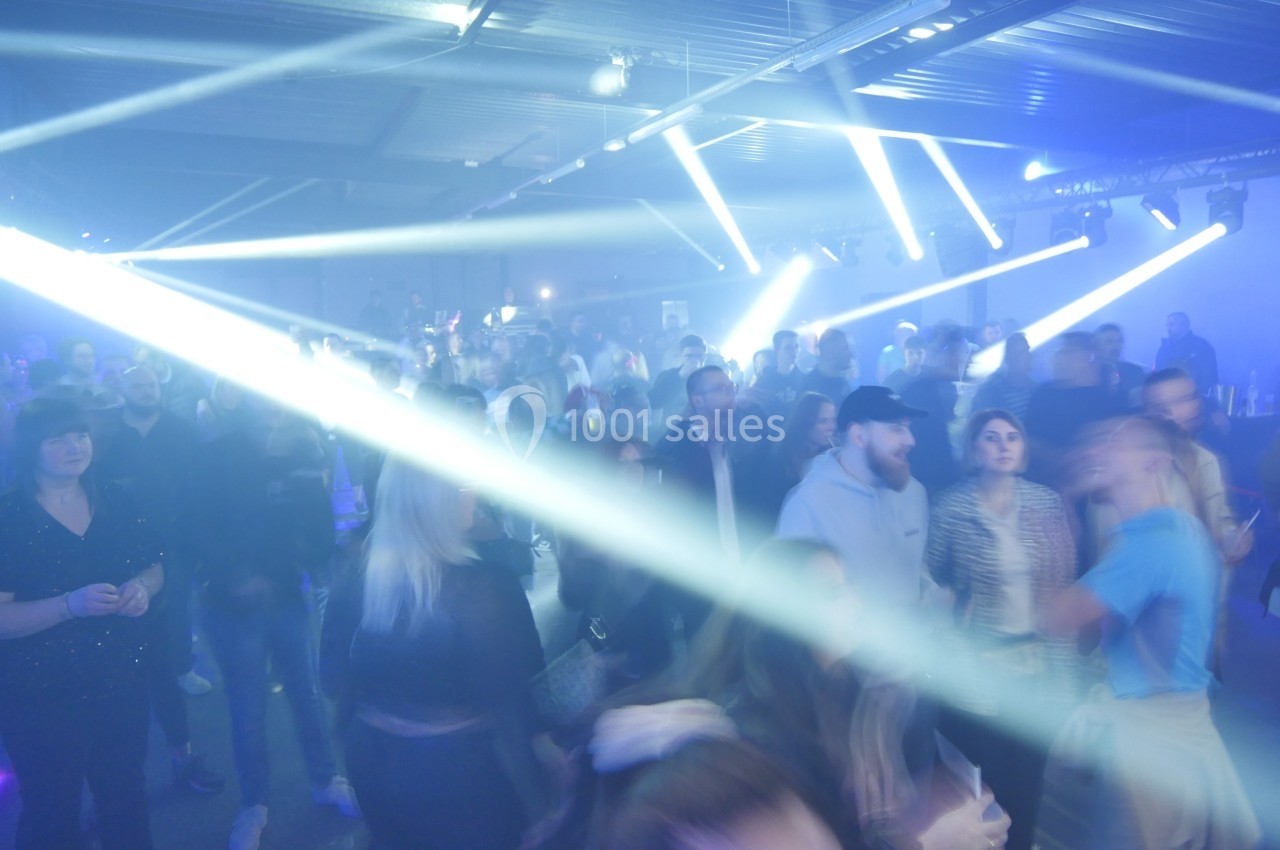 Des personnes dans une salle sombre participent à un événement avec des éclairages lumineux et des faisceaux de lumière.