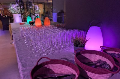 Des enfants colorient des dessins autour d'une table ronde, entourés d'adultes dans un espace intérieur animé.