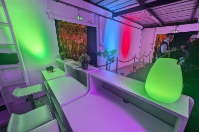 Des enfants colorient des dessins autour d'une table ronde, entourés d'adultes dans un espace intérieur animé.