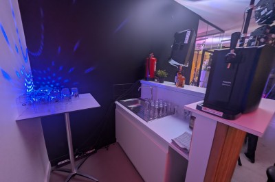 Des enfants colorient des dessins autour d'une table ronde, entourés d'adultes dans un espace intérieur animé.