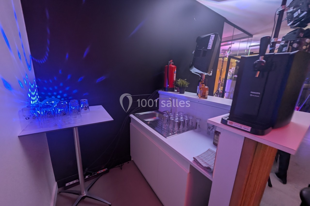 Un coin bar avec évier, verres alignés, machine à bière et éclairage coloré dans une ambiance festive.