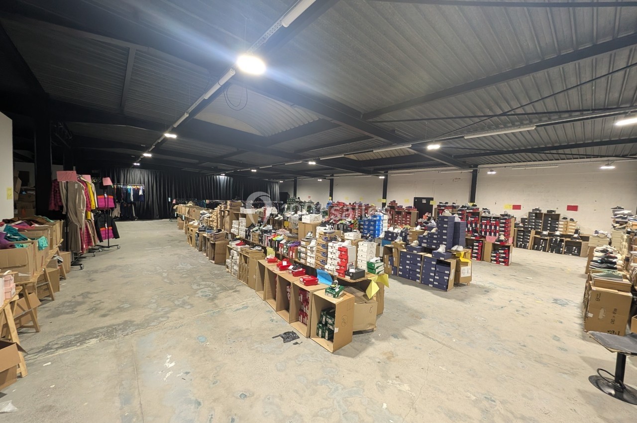 Entrepôt avec des étagères et des cartons contenant des chaussures et vêtements sous un éclairage artificiel.