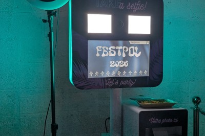 Des enfants colorient des dessins autour d'une table ronde, entourés d'adultes dans un espace intérieur animé.