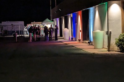 Des enfants colorient des dessins autour d'une table ronde, entourés d'adultes dans un espace intérieur animé.