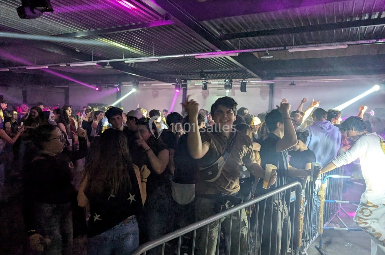 Des personnes dansent et s'amusent dans une salle de concert éclairée par des lumières colorées.