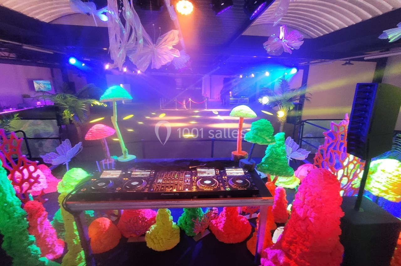 Salle de fête décorée sur le thème sous-marin avec des lumières colorées, une table de mixage et une piste de danse éclairée.