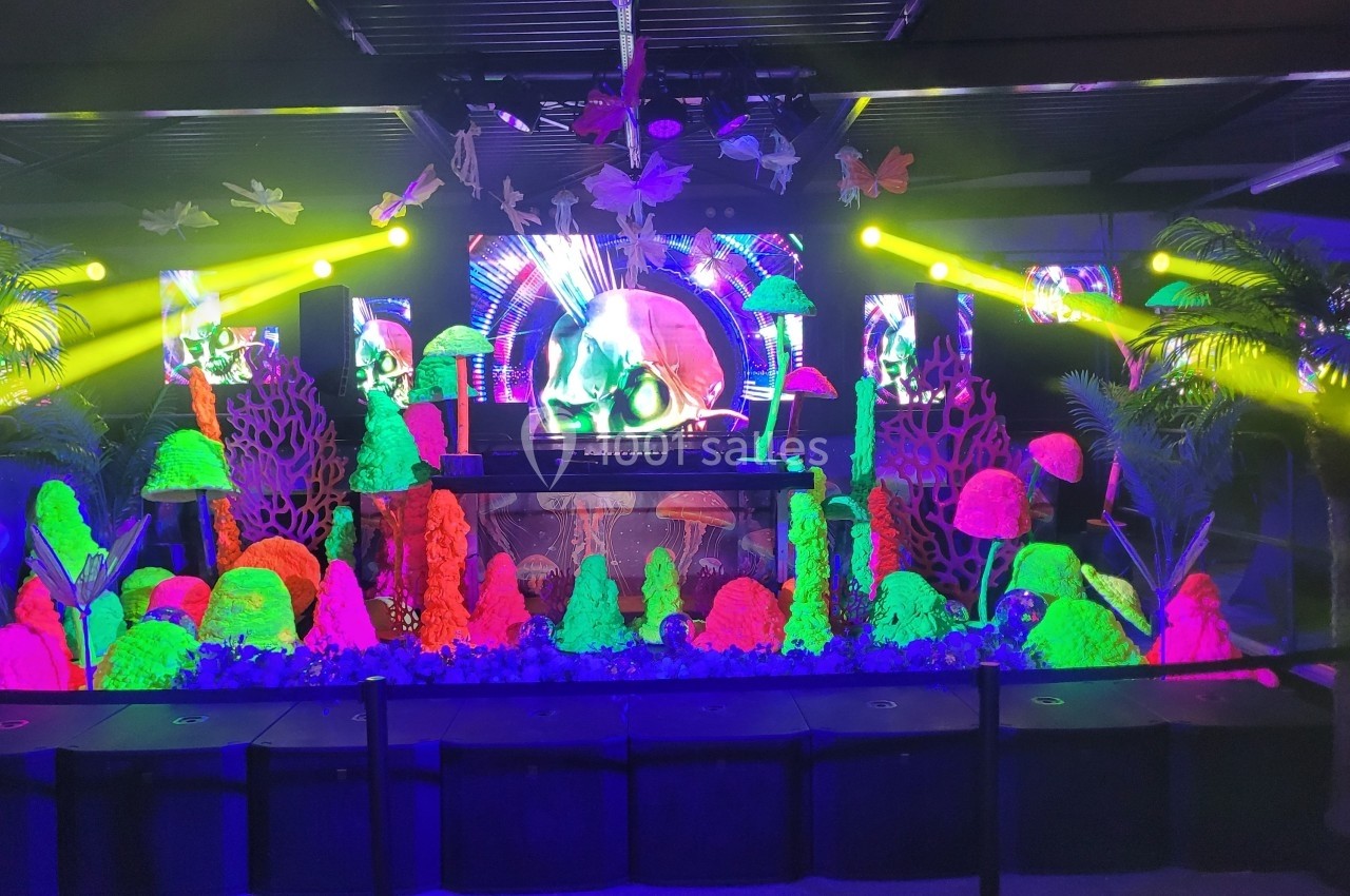 Scène décorée de champignons fluorescents, plantes tropicales et éclairages colorés dans une ambiance festive.