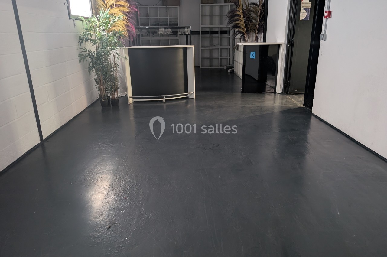 Espace intérieur avec sol sombre, comptoirs clairs, plantes décoratives et étagères en arrière-plan.