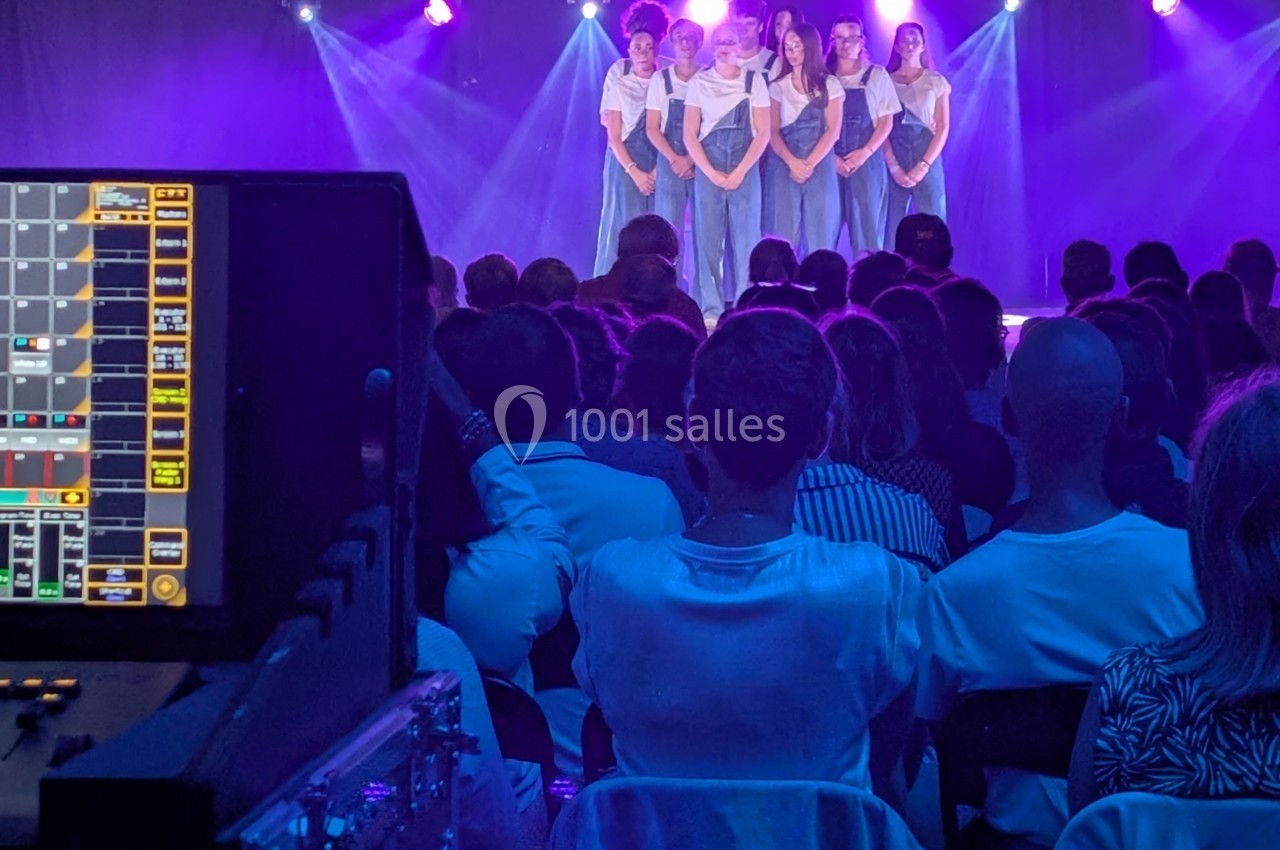 Groupe de jeunes femmes chantant sur scène éclairée de lumières violettes, devant un public assis.