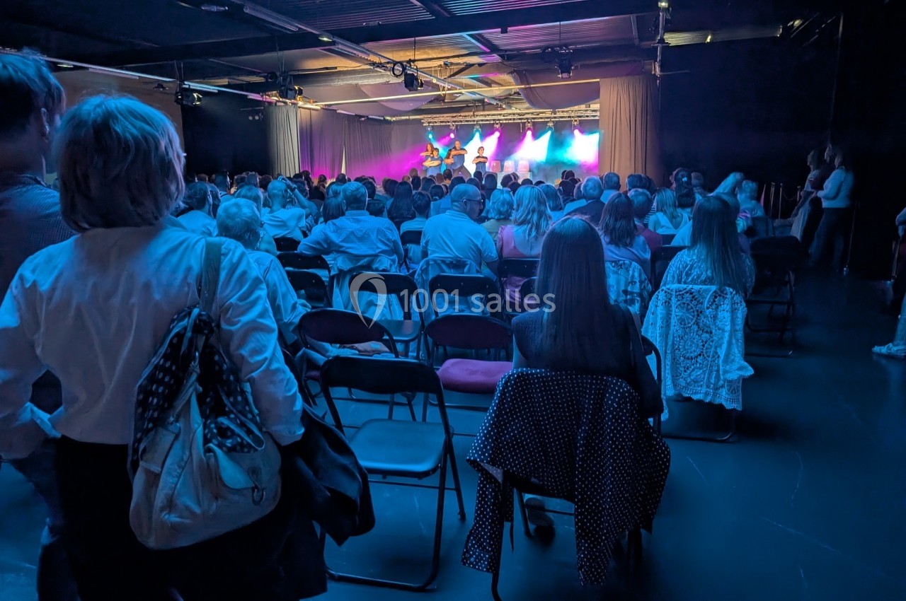 Public assis dans une salle de spectacle sombre, regardant une scène éclairée par des lumières colorées.