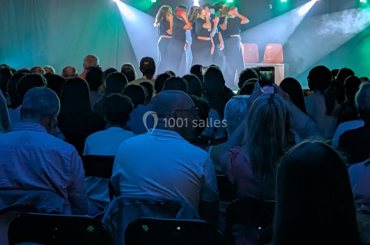 Un groupe de personnes sur scène sous des projecteurs, observé par un public assis dans une salle sombre.