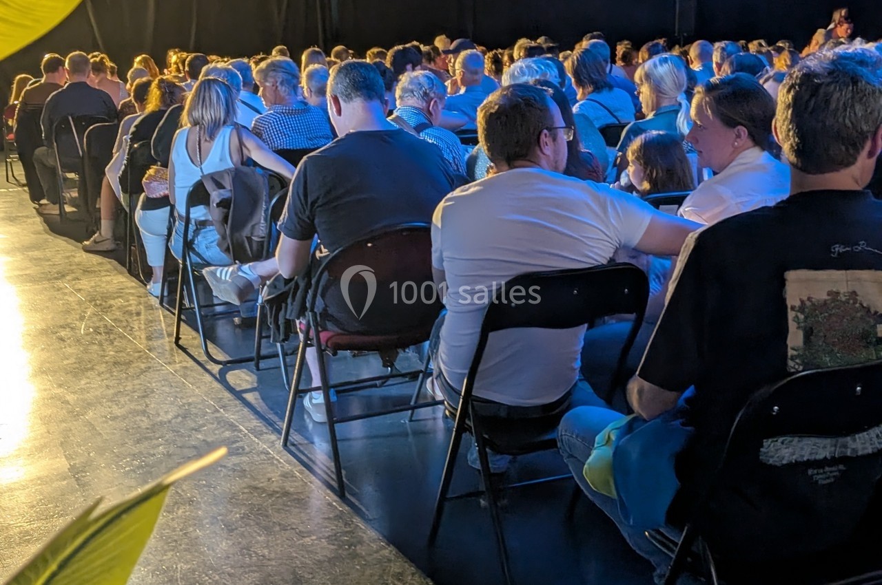 Public assis sur des chaises dans une salle sombre, éclairée par une lumière vive sur le côté.