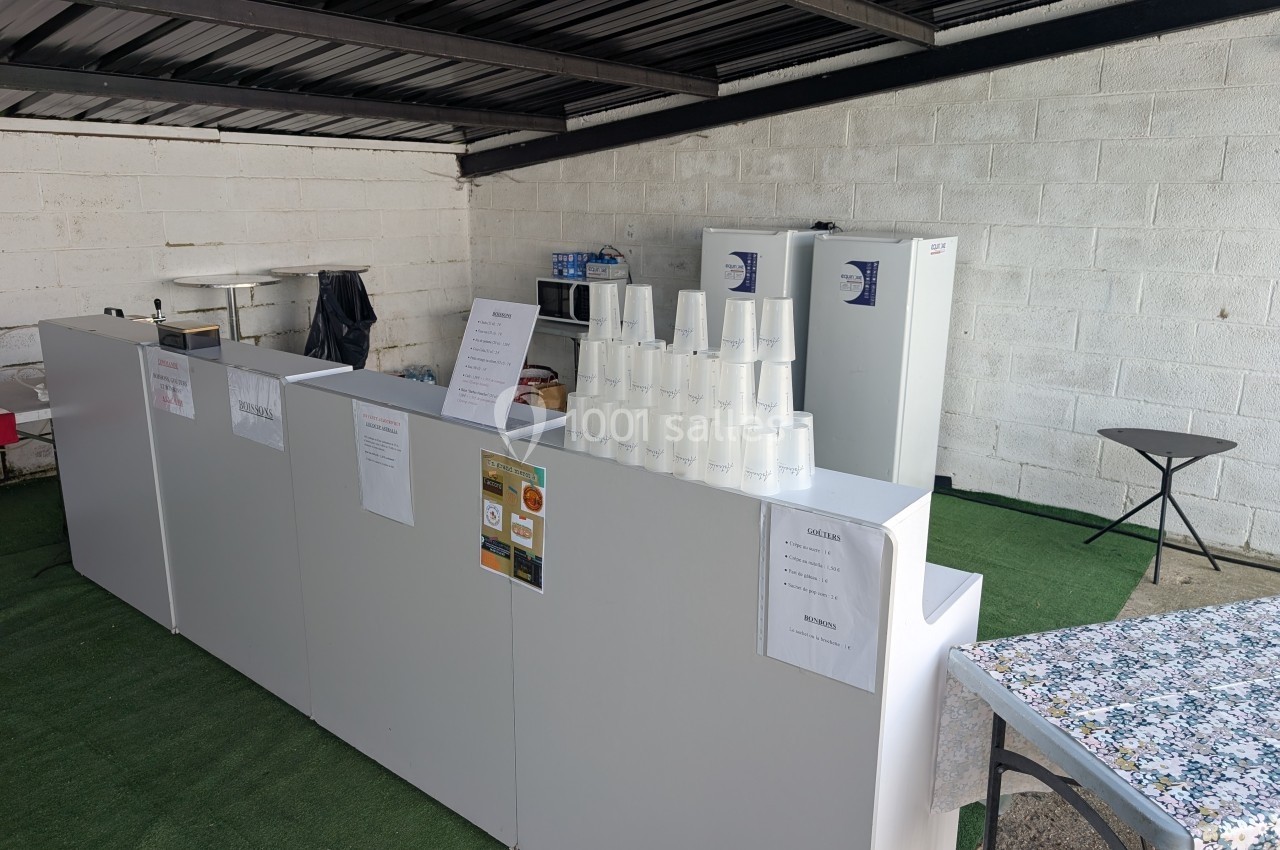 Comptoir blanc avec gobelets empilés, affiches et équipements de cuisine en arrière-plan sous un toit métallique.