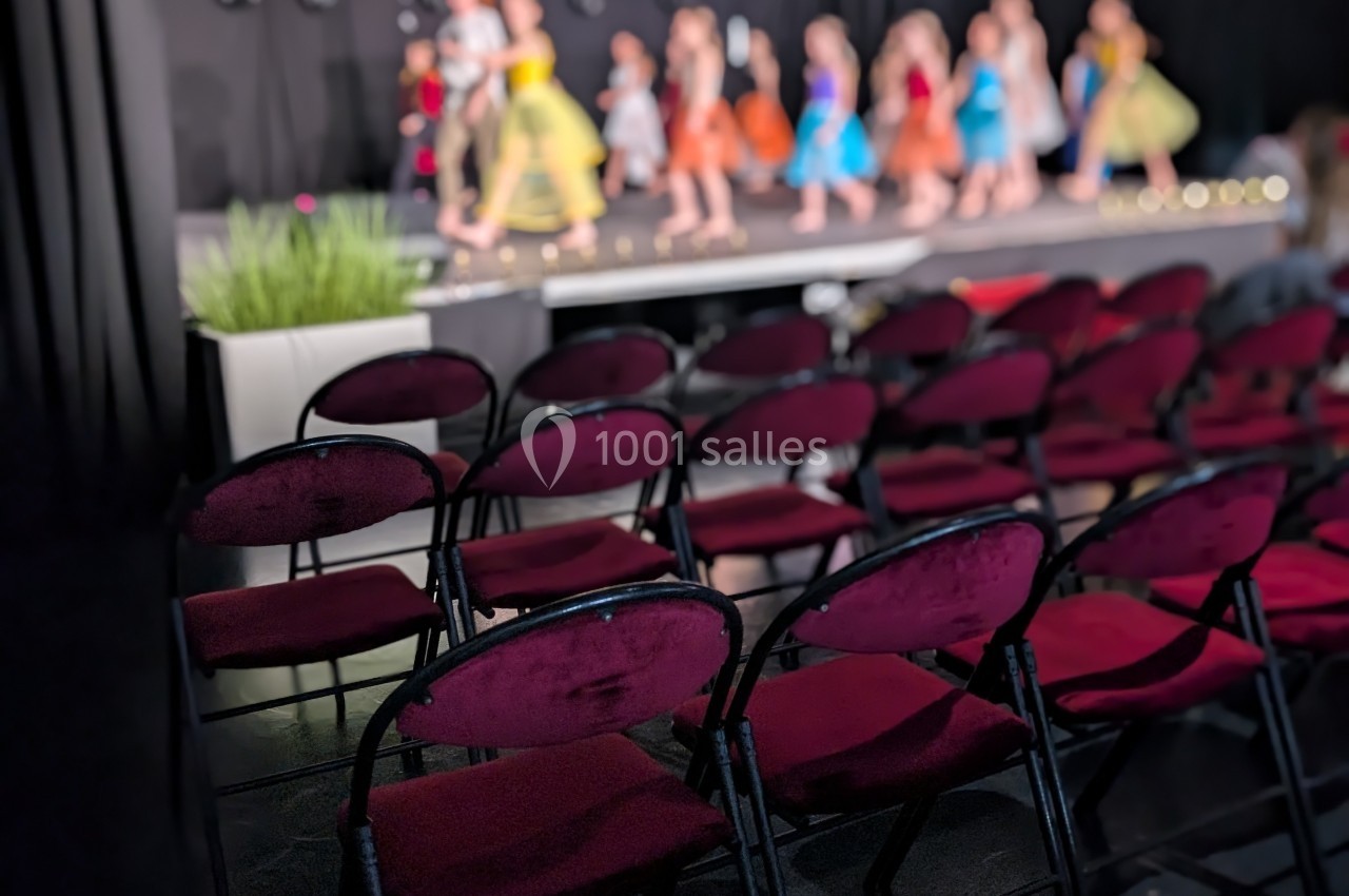 Des chaises rouges vides au premier plan avec des enfants en costume dansant sur une scène en arrière-plan flou.
